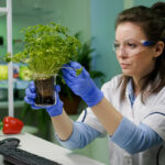 Estudiante de biotecnología en laboratorio utilizando microscopio para investigación científica en salud y medio ambiente.